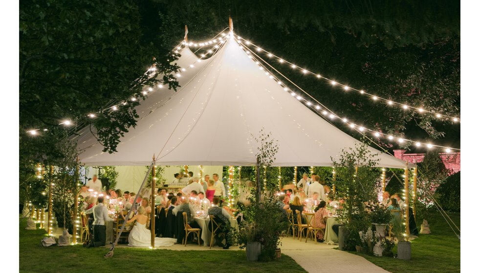 Nighttime view of festoon-lit wedding marquee at Hampshire country garden wedding.