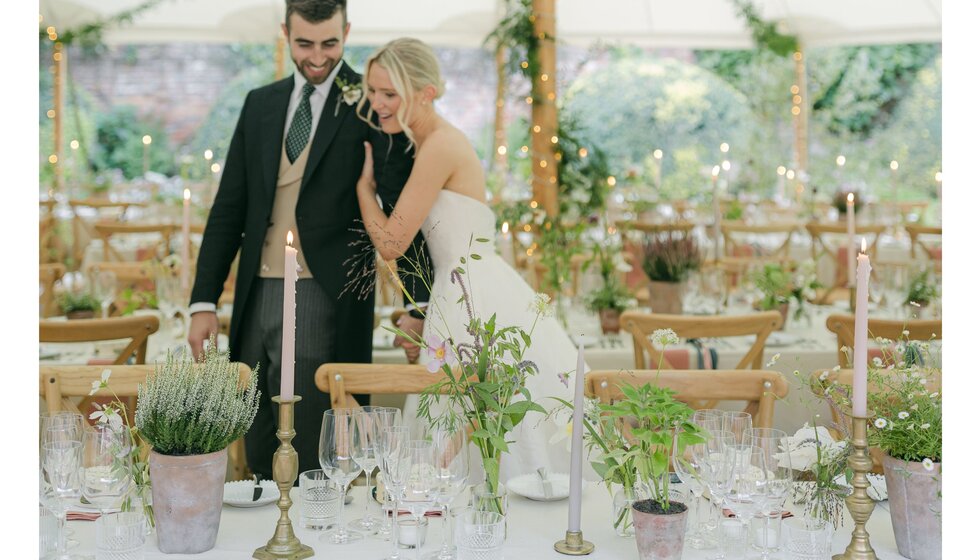 Bride and groom admire country-garden themed table decor in their wedding marquee in Hampshire