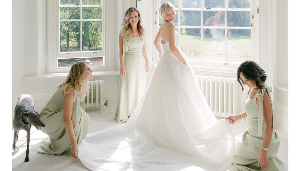 Bridesmaids assist the bride in her sunny bridal suite before the Hampshire country garden wedding.


