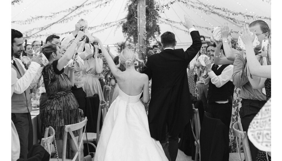 Bride and groom enter the marquee as guests cheer them on in celebration of their English garden wedding in Hampshire.